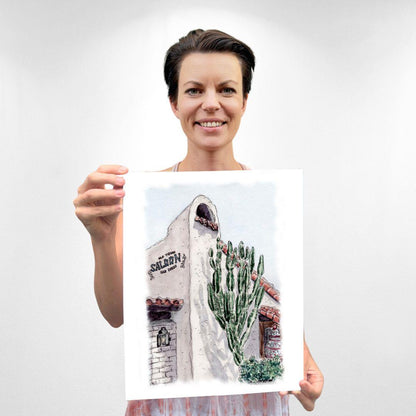 Watercolor print of Old Town San Diego's historic building, featuring a tall cactus and Spanish-style architecture, held by artist Sara. Hand-drawn art with soft pastels and detailed linework by Swil Arts